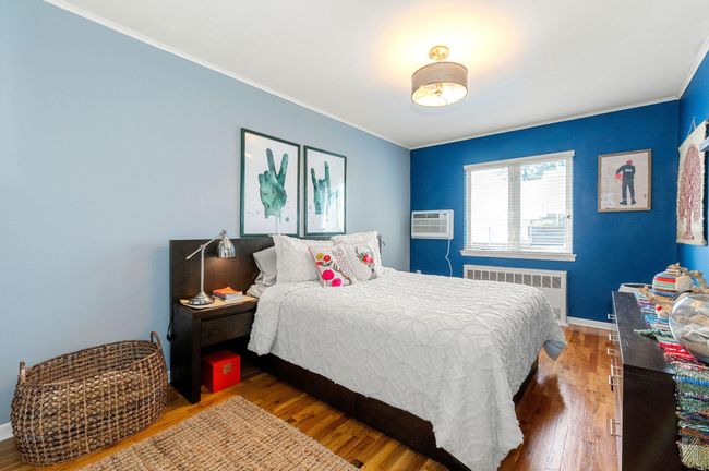 Bedroom with radiator heating unit, ornamental molding, wood finished floors, a wall mounted air conditioner, and baseboards | Image 7