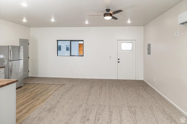 Unfurnished living room featuring light carpet, a wall unit AC, and ceiling fan | Image 35