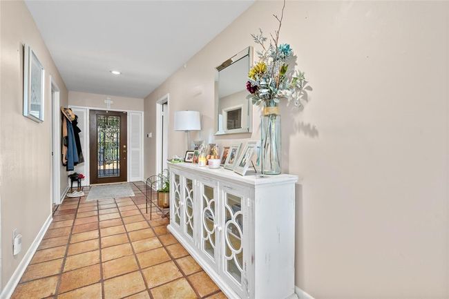 The inviting entryway features warm-toned tile flooring and neutral walls, creating a welcoming atmosphere. A decorative glass-paneled door allows natural light to brighten the space. The hallway offers ample room for décor and storage, setting the perfect first impression for this charming home. | Image 7