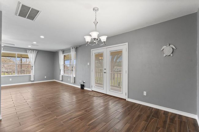 This room features a spacious, open layout with ample natural light from large windows. French doors lead to an outdoor area, and the neutral gray walls create a modern and inviting atmosphere. | Image 14