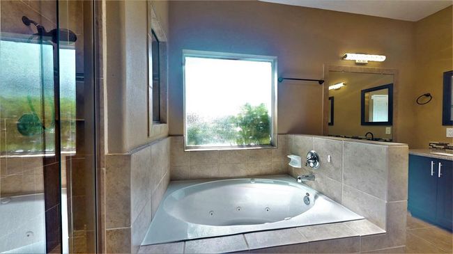 Experience luxury in the 2021-updated primary bathroom featuring double sinks, a jacuzzi tub with steps, a dual shower head, and a large wall mirror. | Image 25