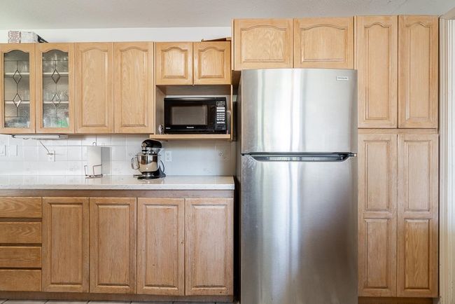 Kitchen with freestanding refrigerator, black microwave, light brown cabinets, and glass insert cabinets | Image 15