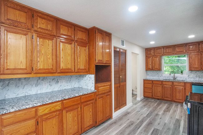 Kitchen with tasteful backsplash, recessed lighting, light wood-style flooring, brown cabinetry, and light stone countertops | Image 13