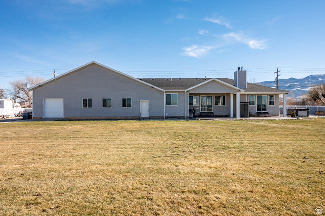 Rear view of property featuring a garage, roof with shingles, a chimney, and a lawn | Image 52