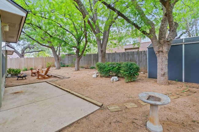 Step outside to a private, fenced-in yard complete with a patio, storage shed, and four mature trees offering a tranquil outdoor setting. | Image 5