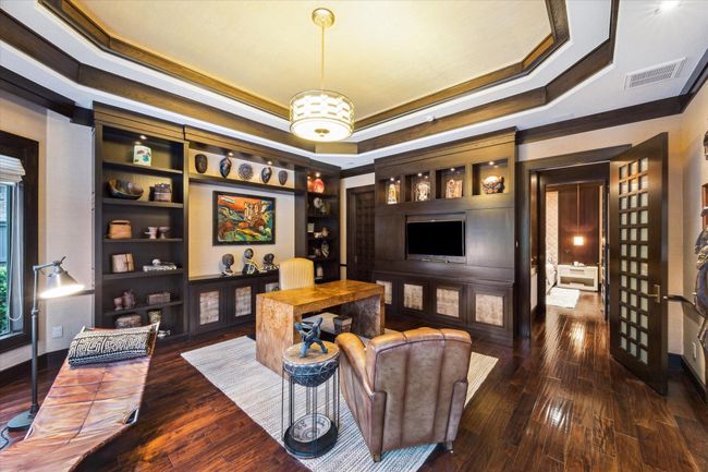 This alternate view of the sophisticated 18’ x 18’ home office highlights richly stained custom built-ins with integrated accent lighting, a media-ready display wall, and a generously sized walk-in closet through the 8-foot custom wood and milk glass door. With direct access to the adjacent bedroom, the space is thoughtfully designed for productivity or relaxing in peace. A perfect balance of function and refinement, it adapts effortlessly, making this space truly versatile. | Image 22