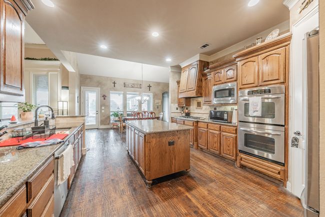 Kitchen featuring appliances with stainless steel finishes, dark wood finished floors, light stone counters, a kitchen island, and backsplash | Image 4