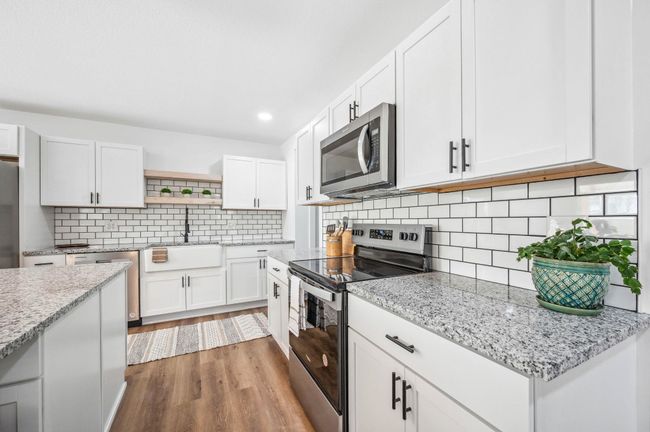 Kitchen with white cabinetry, open shelves, wood finished floors, a sink, and stainless steel appliances | Image 10