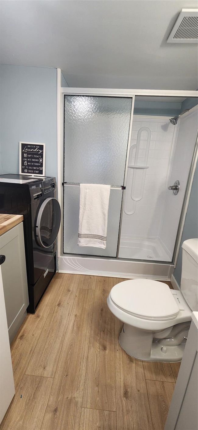 Bathroom featuring a shower with door, toilet, washer / dryer, visible vents, and wood finished floors | Image 19