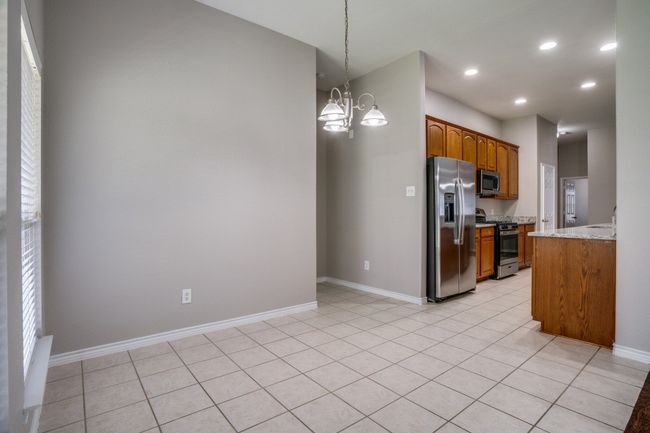 Kitchen with stainless steel appliances, a chandelier, light stone counters, brown cabinets, and recessed lighting | Image 6