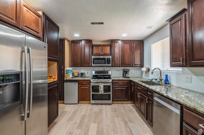 Kitchen featuring appliances with stainless steel finishes, light wood-style floors, light stone countertops, and dark brown cabinetry | Image 23