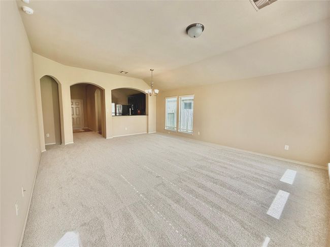 Bright and spacious living area with neutral carpeting, arched entryways, and ample natural light from large windows. Adjacent kitchen with a pass-through window adds convenience. | Image 11