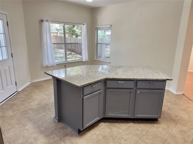 Kitchen with gray cabinets, light stone counters, light tile patterned floors, and a kitchen island | Image 8