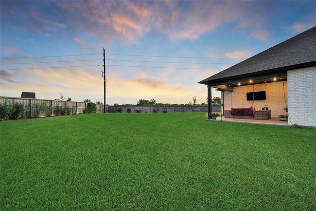 Spacious backyard with lush green lawn, cozy covered patio featuring string lights, and a serene sunset view—ideal for relaxation and outdoor entertaining. | Image 43