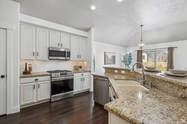 Kitchen with light stone countertops, pendant lighting, white cabinetry, appliances with stainless steel finishes, and sink. Plantation shutters | Image 6