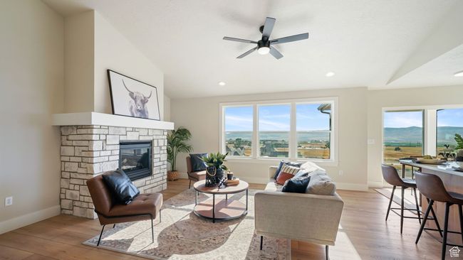 Living area featuring light wood-type flooring, a ceiling fan, a stone fireplace, vaulted ceiling, and recessed lighting | Image 5