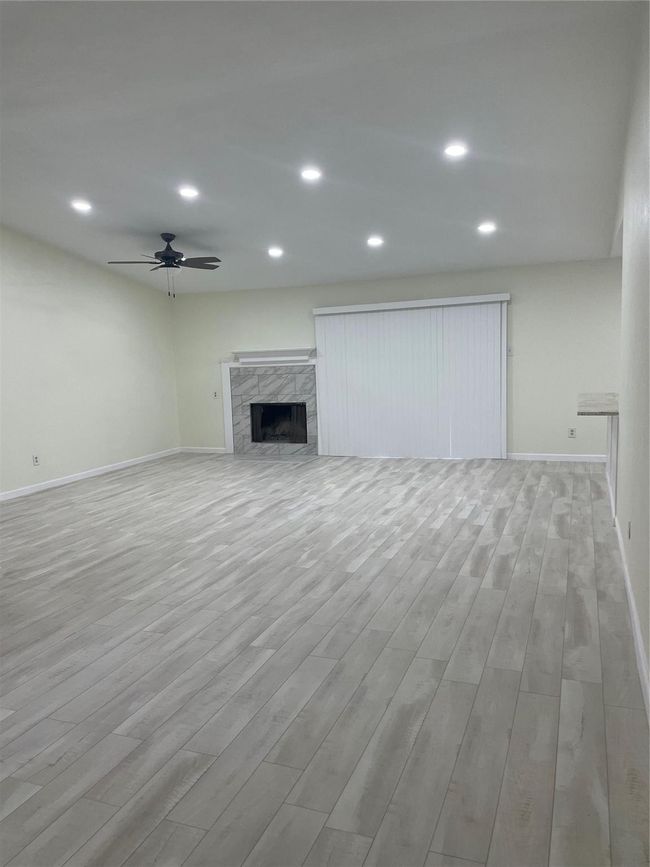 Unfurnished living room with wood finished floors, a fireplace, a ceiling fan, baseboards, and recessed lighting | Image 26