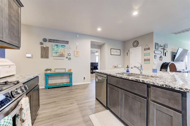 Kitchen with stainless steel appliances, dark brown cabinetry, ceiling fan, light stone counters, and recessed lighting | Image 17