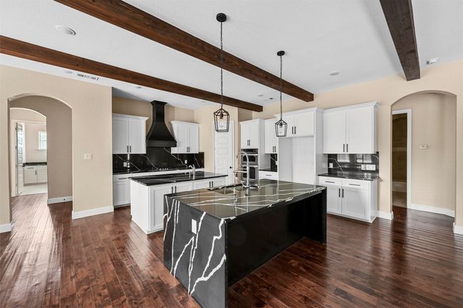 Kitchen with tasteful backsplash, a center island with sink, arched walkways, dark countertops, and custom exhaust hood | Image 24