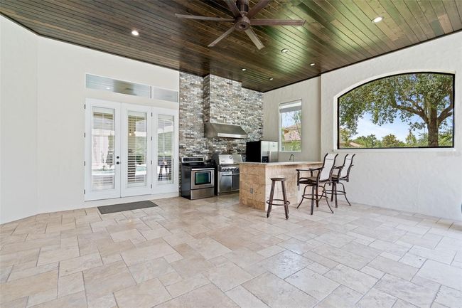 The outdoor kitchen is a showstopper, complete with a full-size refrigerator, grill, range, dishwasher, sink, bar seating, and stone accent wall—all under a richly finished wood ceiling. | Image 26