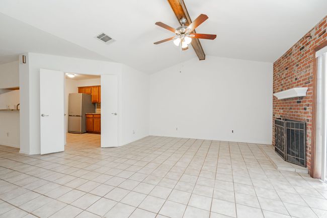 Unfurnished living room featuring light tile patterned floors, ceiling fan, lofted ceiling with beams, a fireplace, and visible vents | Image 15