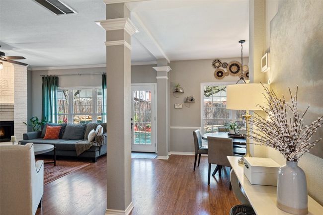 Dining space featuring a ceiling fan, dark wood-type flooring, a brick fireplace, ornamental molding, and ornate columns | Image 15