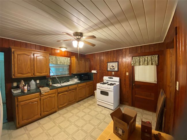 Kitchen featuring white gas range, light floors, wooden walls, a ceiling fan, and brown cabinets | Image 14