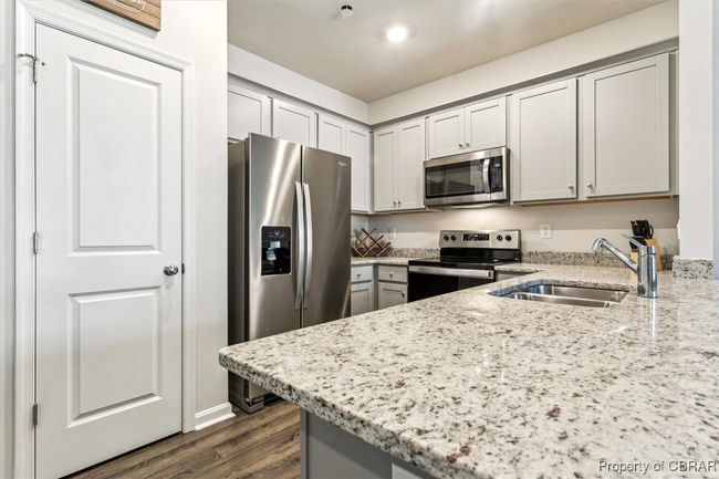 Kitchen with a sink, light stone countertops, gray cabinetry, appliances with stainless steel finishes, and dark wood-style flooring | Image 5