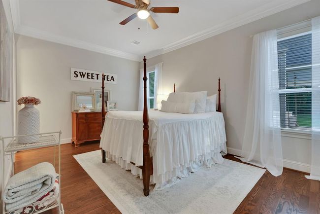 A convenient downstairs secondary bedroom is privately situated toward the back of the home, located just behind the garage—ideal for guests or multi-generational living. This room features tall ceilings, double crown moulding, and 2-inch blinds, creating a refined yet comfortable atmosphere. | Image 20