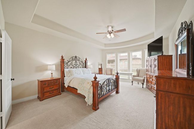 This spacious bedroom features a cozy carpeted floor, elegant tray ceiling, and large windows offering ample natural light. | Image 19