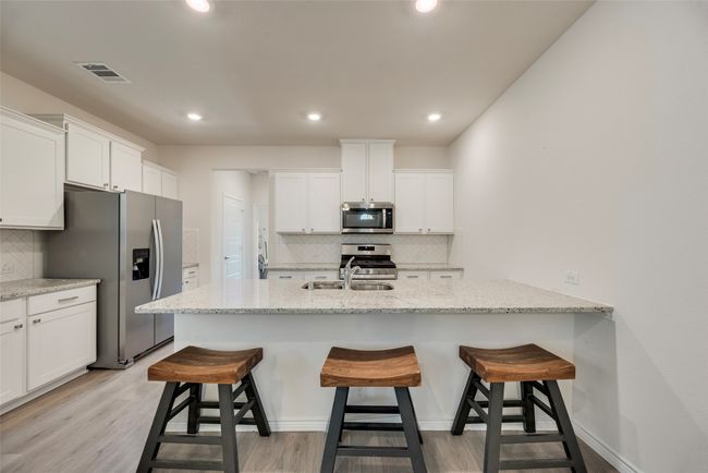 Kitchen featuring stainless steel appliances, tasteful backsplash, white cabinetry, a breakfast bar, and recessed lighting | Image 17