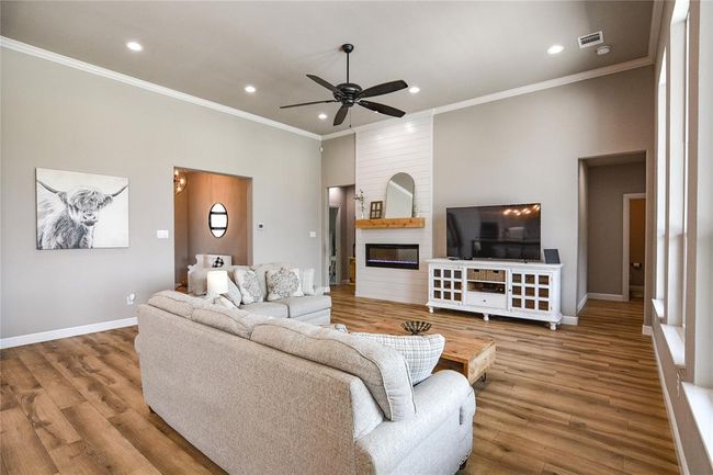 Living room with crown molding, wood-type flooring, a large fireplace, and ceiling fan | Image 14