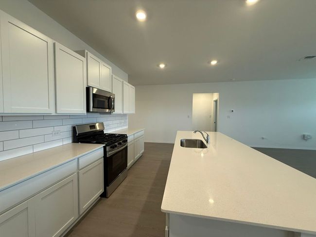 Kitchen featuring appliances with stainless steel finishes, a sink, backsplash, a center island with sink, and dark wood-style floors | Image 20