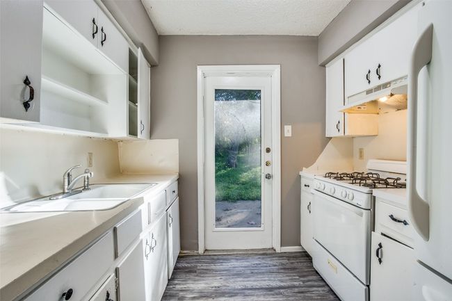 Kitchen featuring white cabinets, a sink, white appliances, wood finished floors, and under cabinet range hood | Image 9