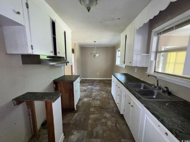 Kitchen with a sink, stone finish floors, dark countertops, white cabinetry, and baseboards | Image 5