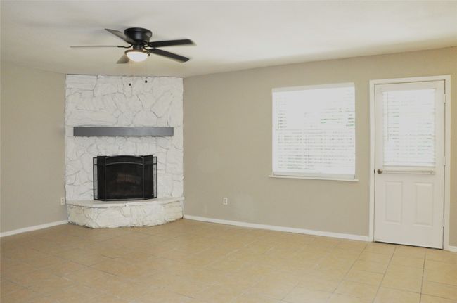 Unfurnished living room with baseboards, a ceiling fan, a stone fireplace, and plenty of natural light | Image 8