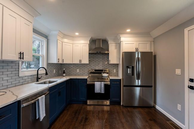 Kitchen featuring dark wood-type flooring, wall chimney range hood, blue cabinets, appliances with stainless steel finishes, and a sink | Image 8
