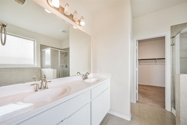 This primary bathroom features a double sink vanity with modern fixtures, a large mirror, and ample natural light. There's a walk-in closet and a glass-enclosed shower, offering a clean and spacious layout. | Image 11