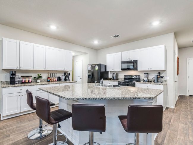 Kitchen featuring visible vents, light wood finished floors, a sink, black appliances, and a kitchen breakfast bar | Image 6