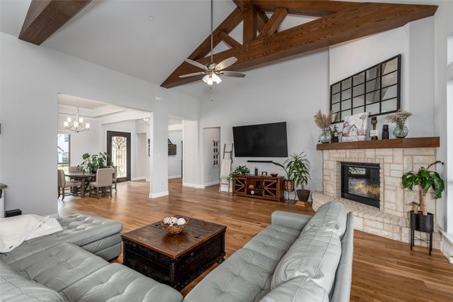 Living area with high vaulted ceiling, a ceiling fan, a chandelier, wood finished floors, and a stone fireplace | Image 9