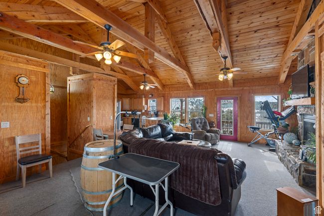 Living room featuring wood walls, wooden ceiling, lofted ceiling with beams, a stone fireplace, and carpet floors | Image 19