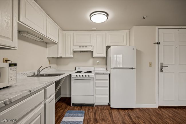 Kitchen with a sink, under cabinet range hood, dark wood-type flooring, white appliances, and white cabinets | Image 5