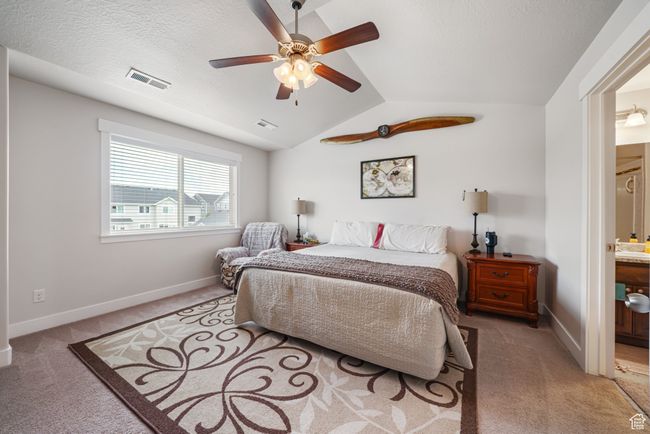 Bedroom featuring light colored carpet, vaulted ceiling, connected bathroom, and a ceiling fan | Image 14