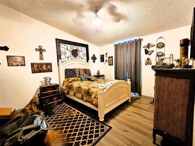 Bedroom featuring a textured ceiling, wood finished floors, vaulted ceiling, a ceiling fan, and baseboards | Image 19