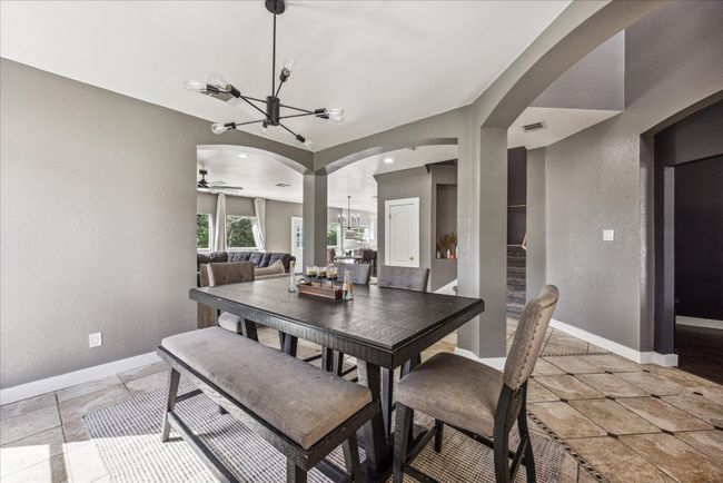 Dining space with arched walkways, baseboards, ceiling fan with notable chandelier, stairway, and a textured wall | Image 7