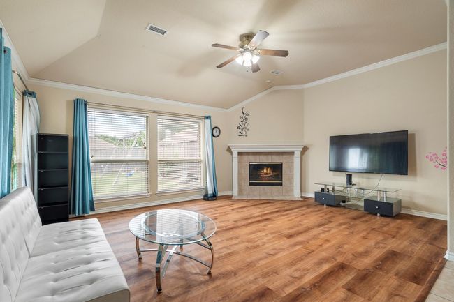 Living room featuring vaulted ceiling, ceiling fan, wood finished floors, a fireplace, and ornamental molding | Image 21