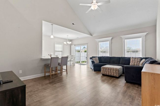 Living room featuring ceiling fan with notable chandelier, lofted ceiling, wood finished floors, and visible vents | Image 8