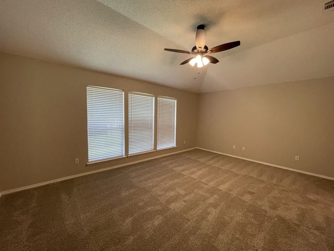 Empty room with dark carpet, a ceiling fan, a textured ceiling, and vaulted ceiling | Image 6