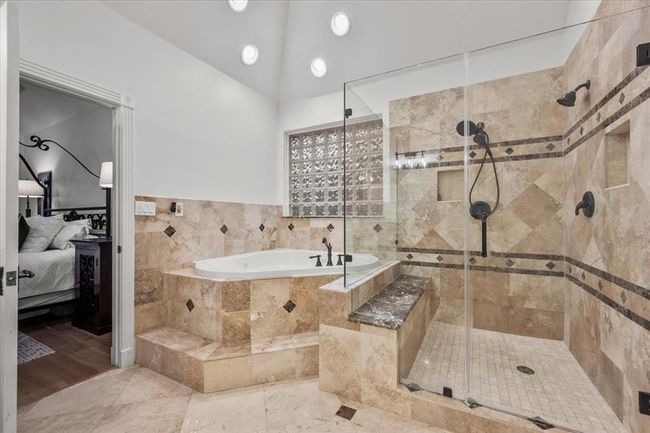 The glass-enclosed walk-in shower is oversized and beautifully designed, offering dual showerheads, bench seating, and gorgeous tile throughout. | Image 24