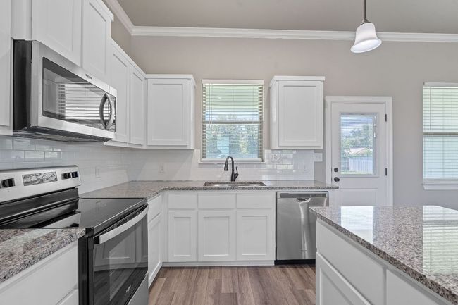 Kitchen with appliances with stainless steel finishes, ornamental molding, white cabinets, light wood-style floors, and backsplash | Image 15
